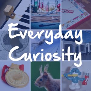 The words "Everyday Curiosity" appear in white handwriting over a collage of nine images (a cardboard figure playing the piano, a close-up of a playground swing, the corner of a Monopoly board, an oscillating fan, an underwater shot of swimmers, air conditioners on the site of a building, a gold medal, a squirrel with furry ears, and a smurf figurine brushing its teeth)
